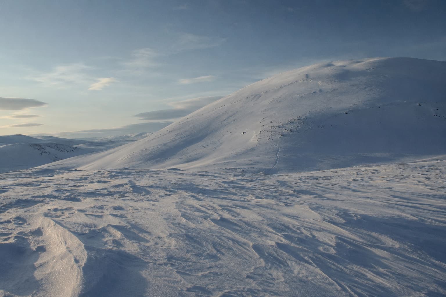 Snötäckta fjäll med vindpackad snö och ett svagt uppåtspår